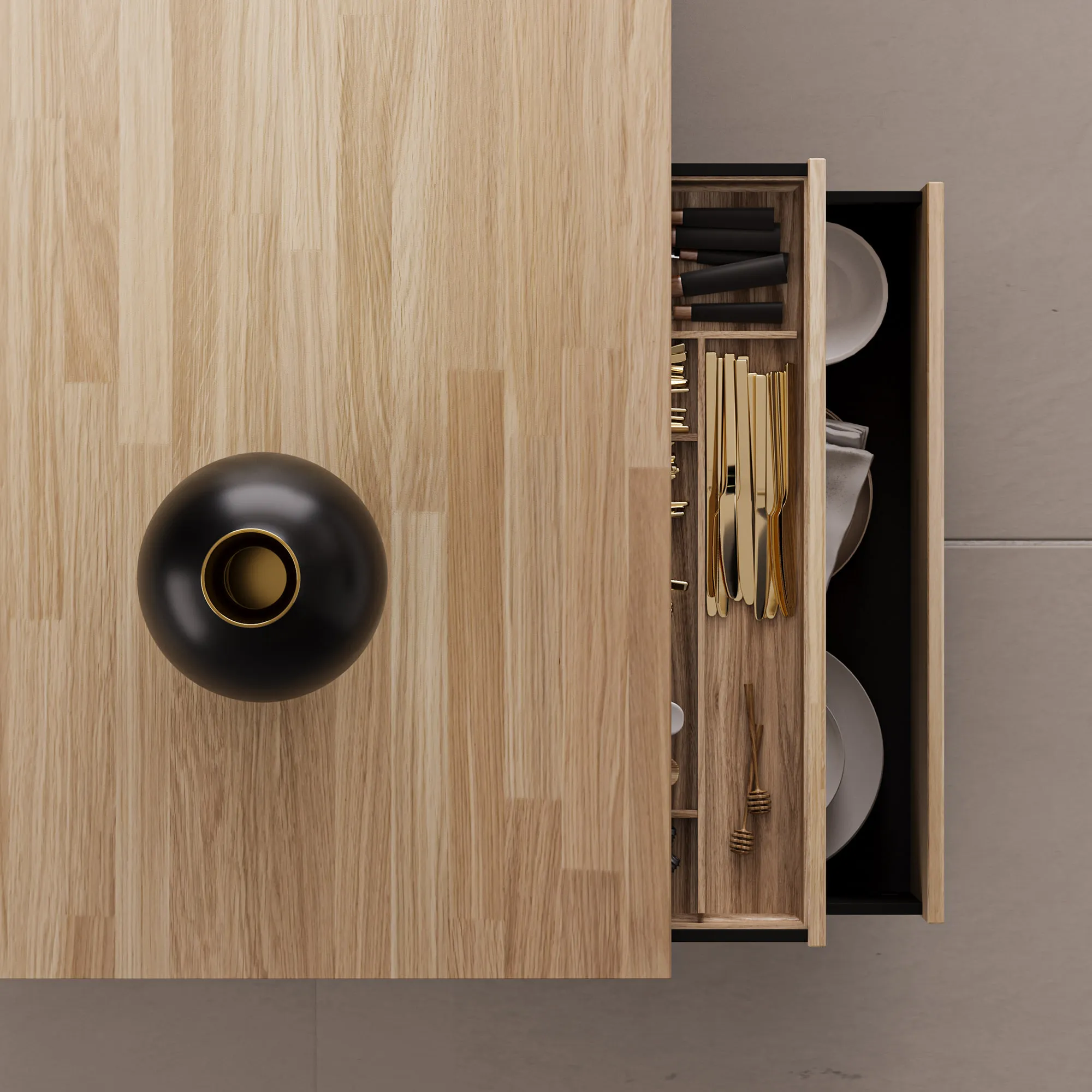 Overhead detail of an oak worktop and open drawer, brass cutlery laid in a wooden insert above a compartment of white plates.