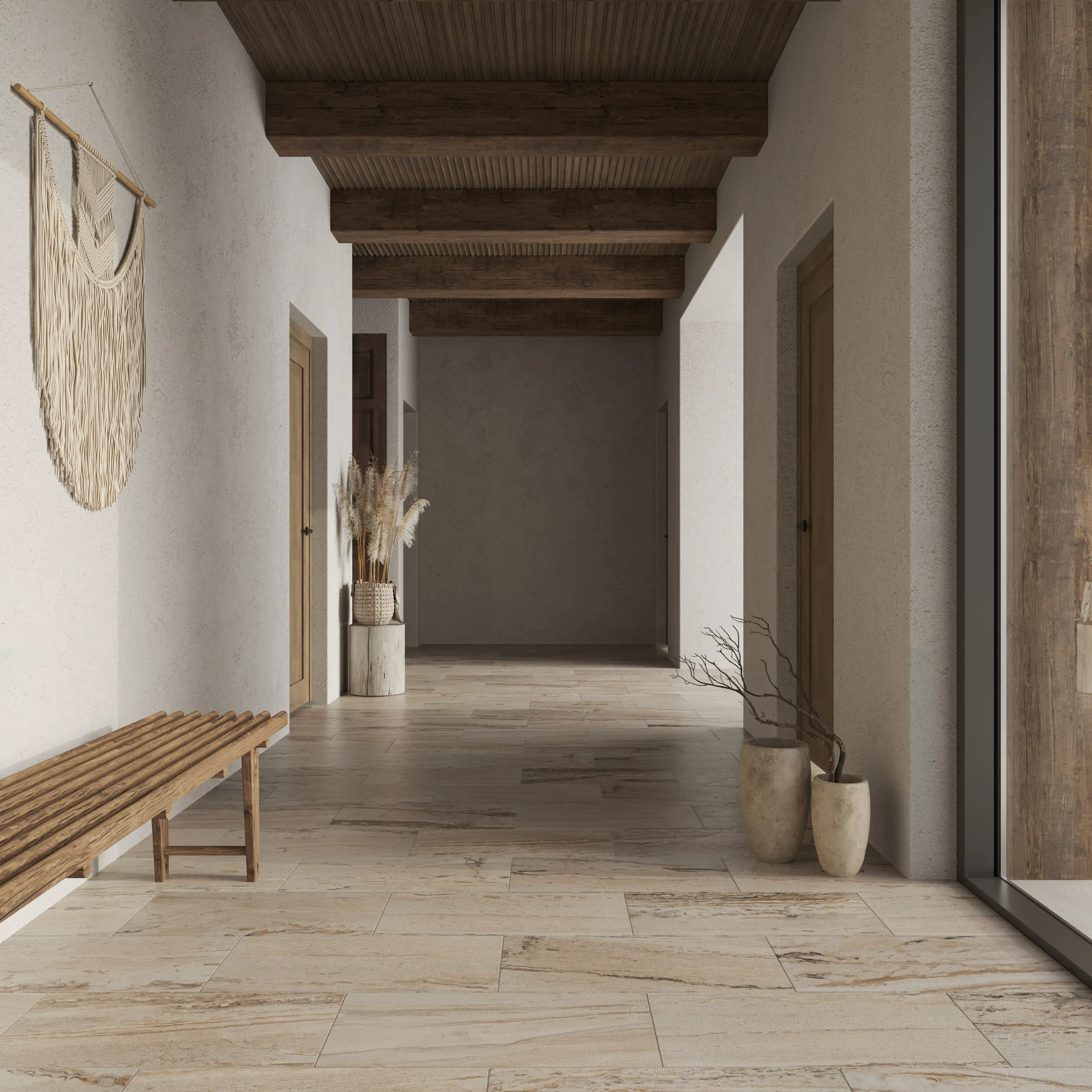 Hallway floored in large-format travertine-look porcelain under an exposed timber beam ceiling, with a wooden bench and dried grasses in tall vases.