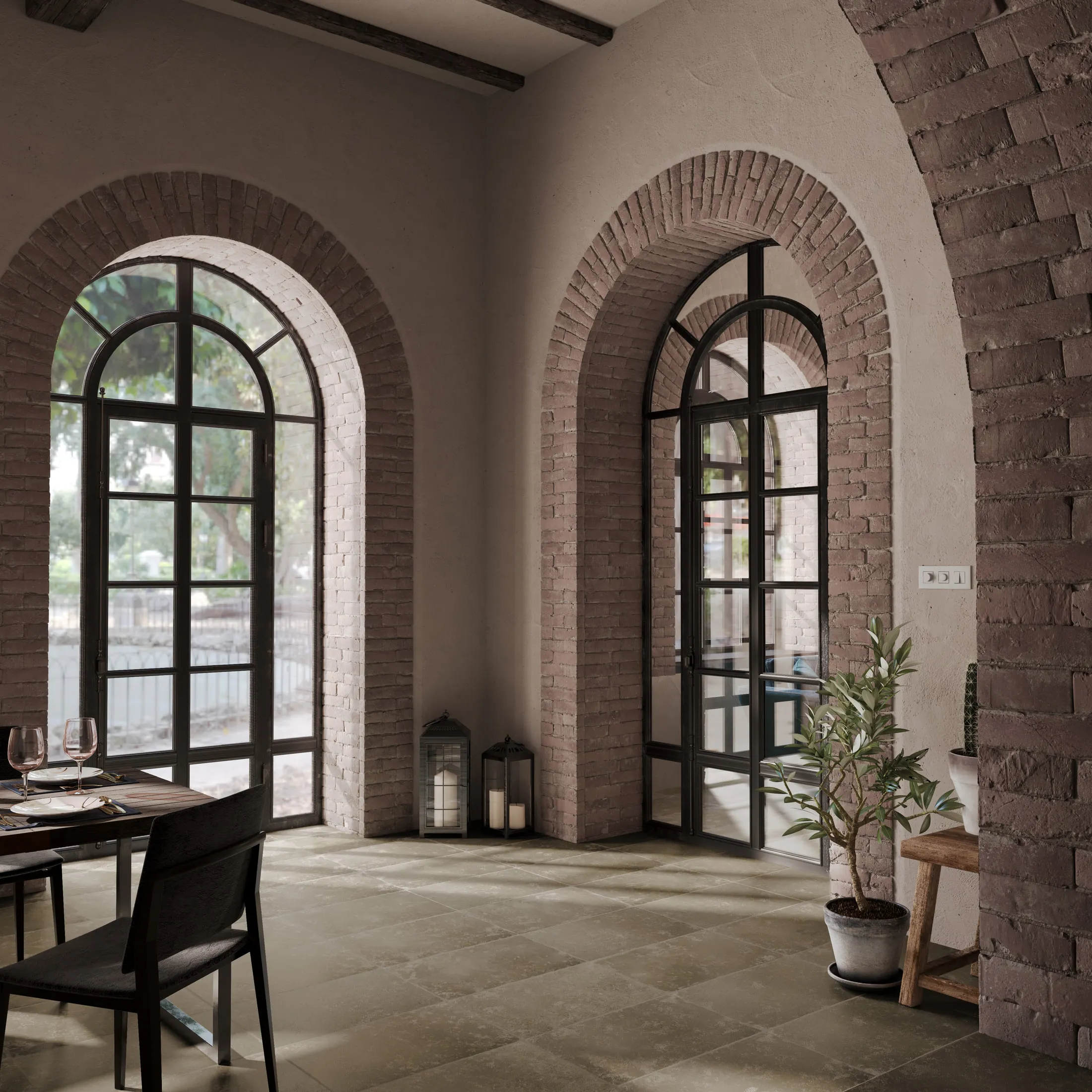 Dining room with limestone-beige floor tile running to exposed brick arches and black steel arched windows, with a potted olive tree.