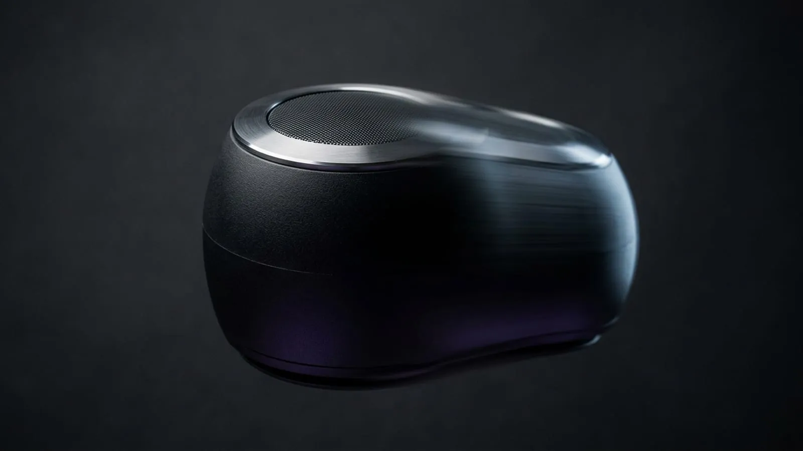 A matte black wireless speaker photographed mid-rotation against a dark studio backdrop, its trailing edge smeared into motion blur while the leading edge stays sharp.