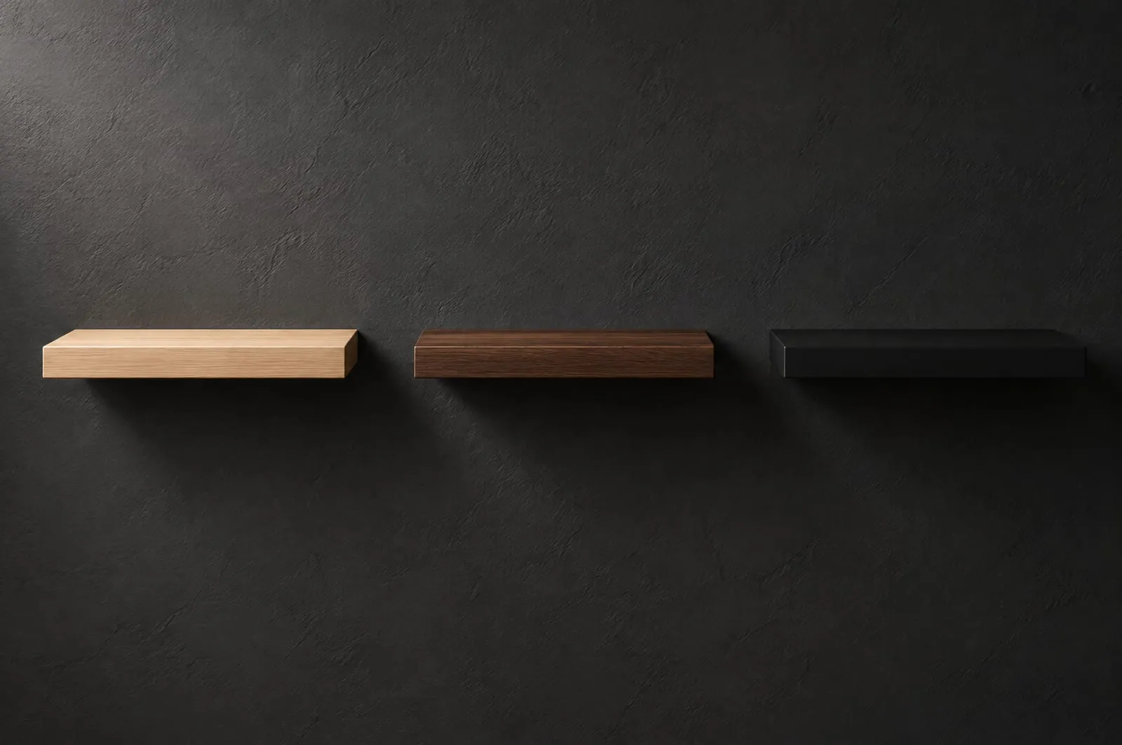 Three identical floating wall shelves side by side on a dark wall, in pale white oak, dark walnut and matte black, each lit from the same angle.